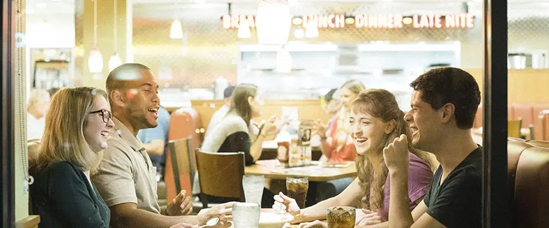 A group of people happily chatting while eating at a Denny's restaurant