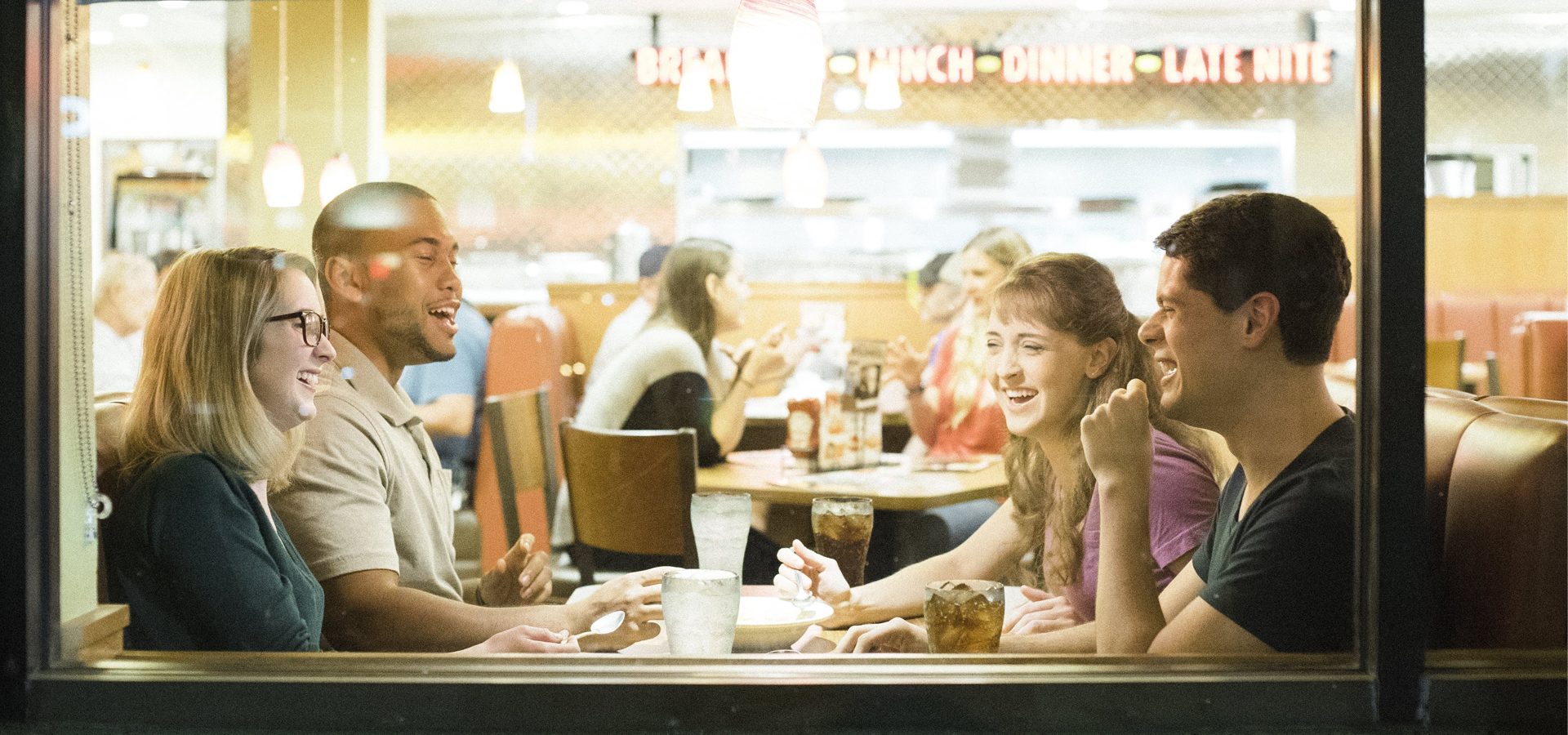 A group of people happily chatting while eating at a Denny's restaurant